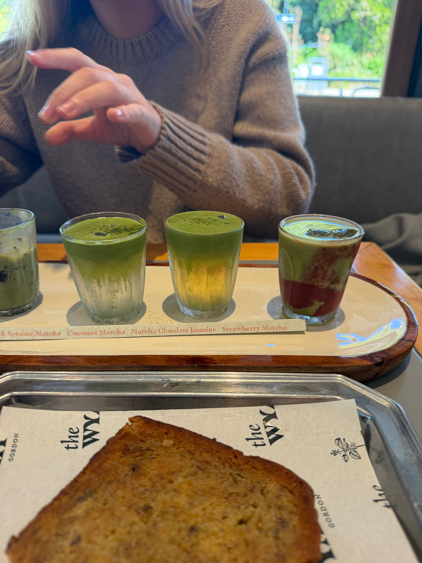 The second half of The Wyatt's winter matcha flight in Gordon, Sydney — Truffle Black Sesame, Coconut, Matcha Cloud on Jasmine and Strawberry Matcha alongside a slice of banana bread on a Wyatt-branded tray.