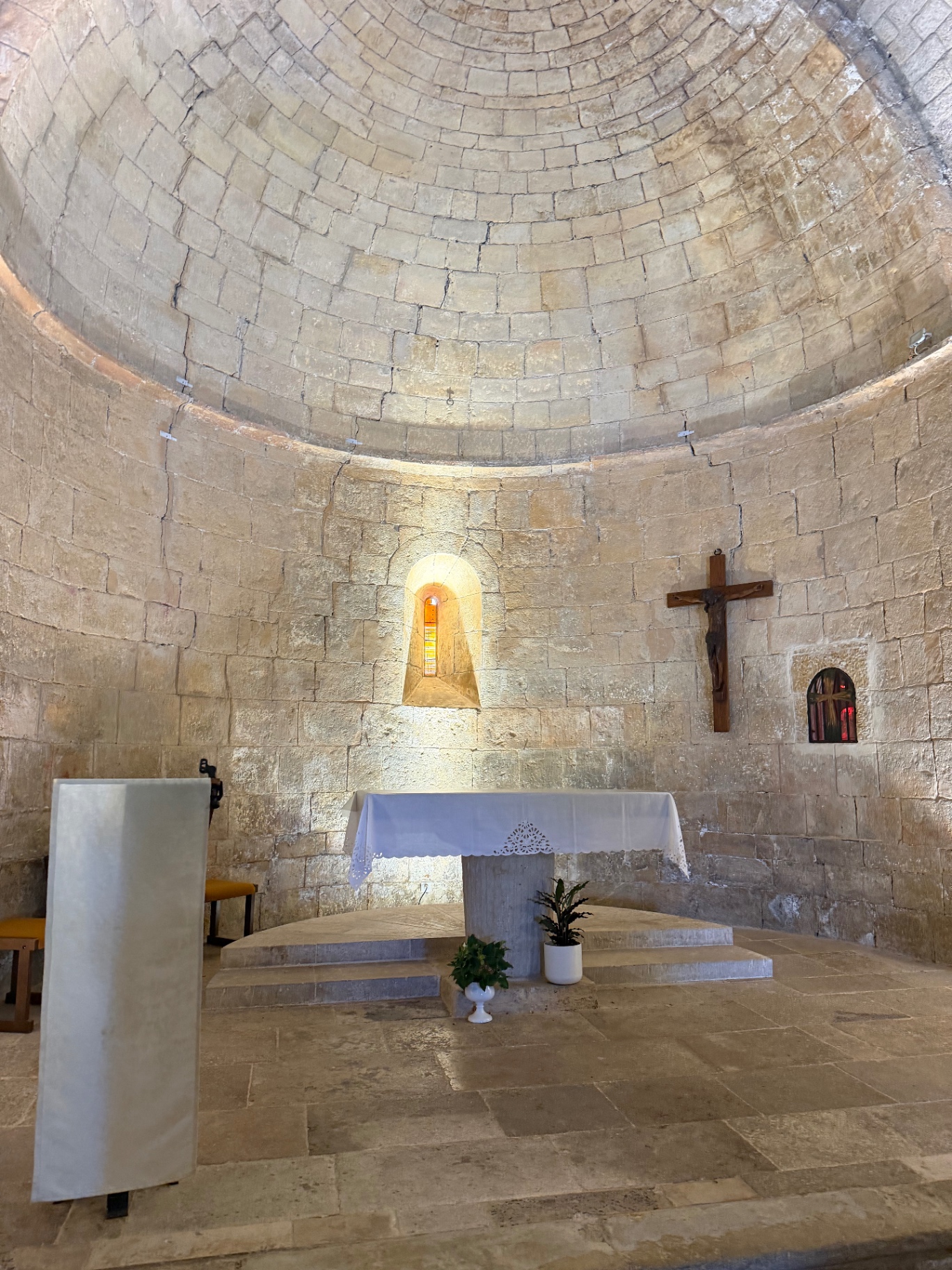 The simple interior of the hilltop church in Tourtour — a domed honey-stone apse with a single arched window, a wooden crucifix on the wall and a linen-draped altar.