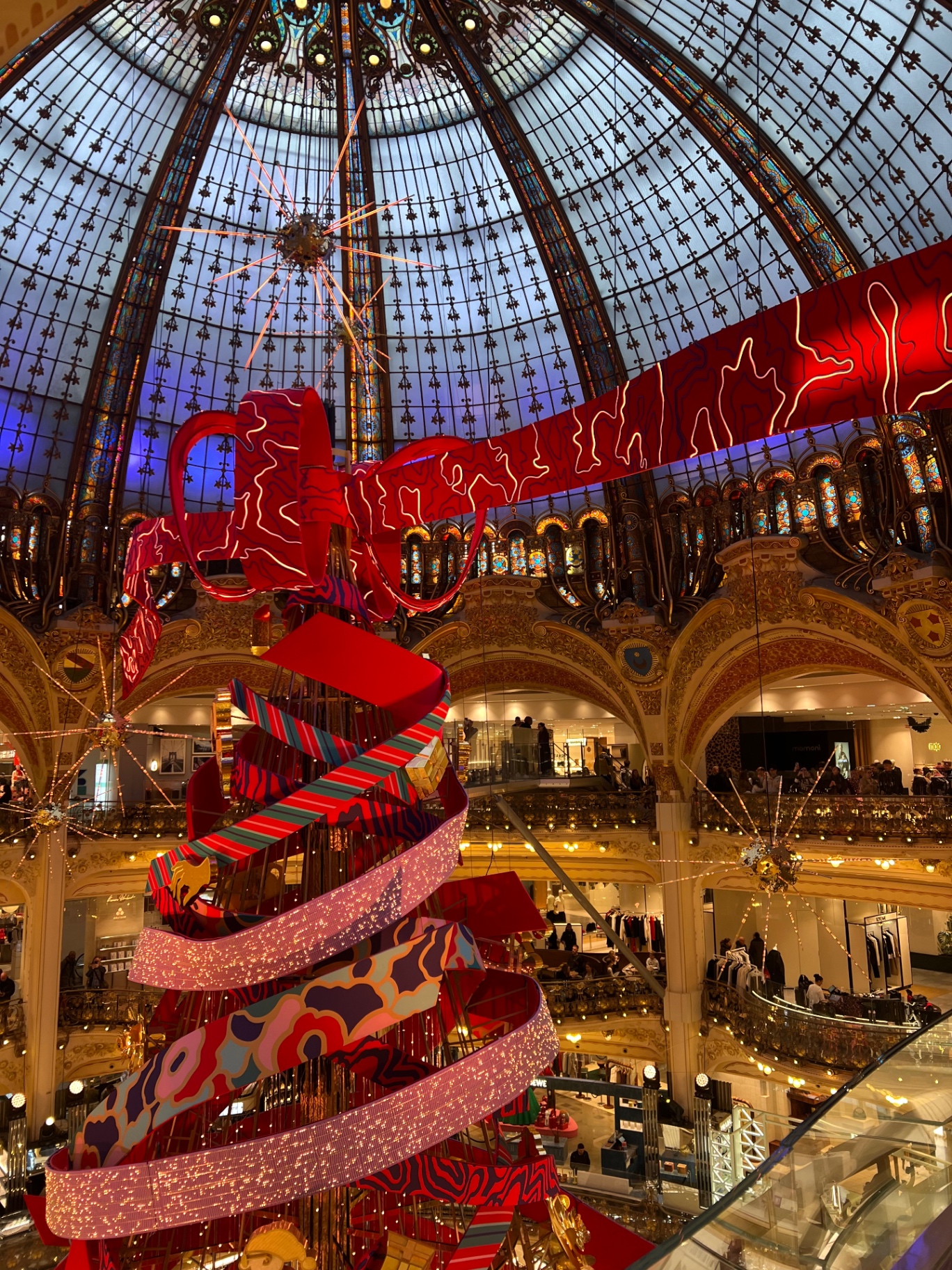 The stained-glass dome of Galeries Lafayette in Paris with the seasonal ribbon Christmas tree suspended beneath it.