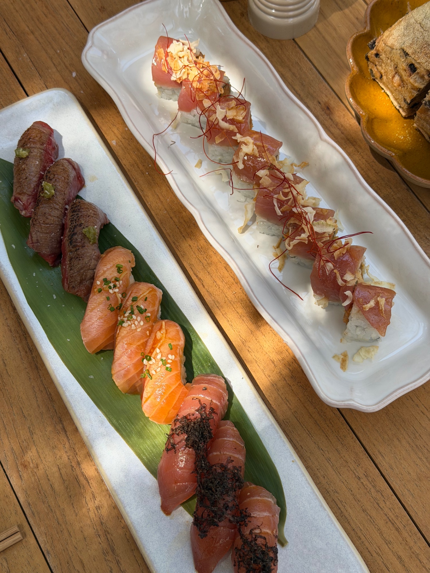 A long plate of nigiri sushi and a maki roll on the table at SALTO, alongside two Aperol spritzes in branded glasses with sliced bread.