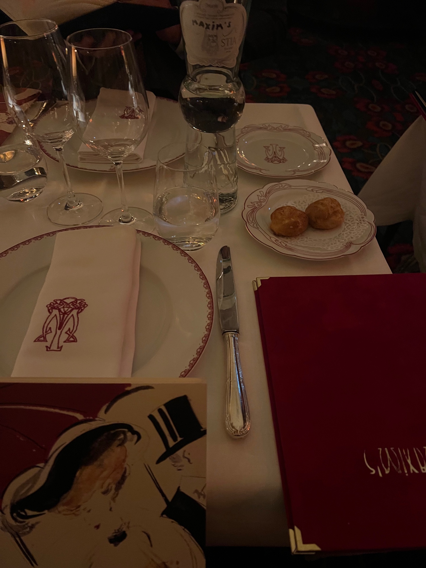 An intimate candlelit table setting at Maxim's in Paris with monogrammed napkins, gougères and the signature red menu.